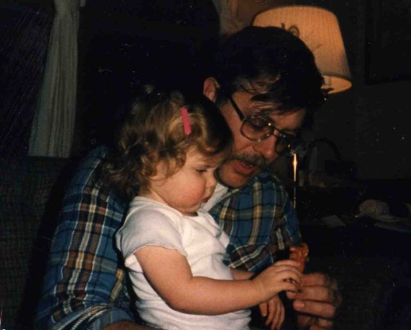 Toddler girl sits on father's lap holding toy in vintage photo