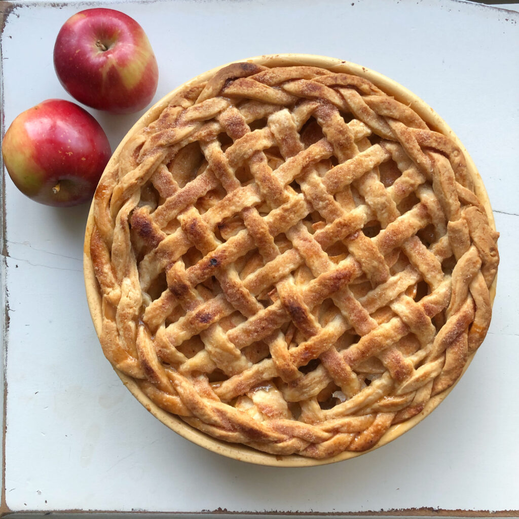 Apple pie with beautiful lattice and braided crust on white table with two apples