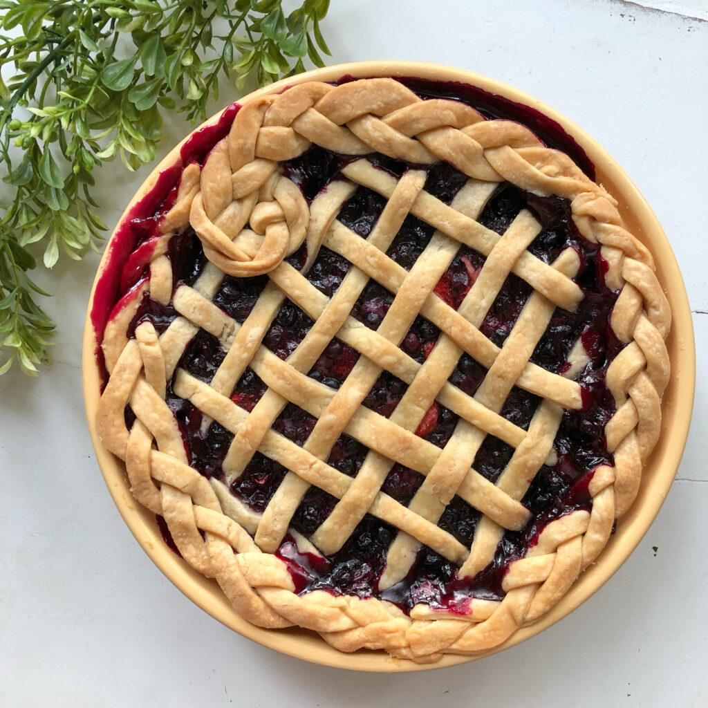 blueberry pie with beautiful lattice and braided crust on white table with greenery