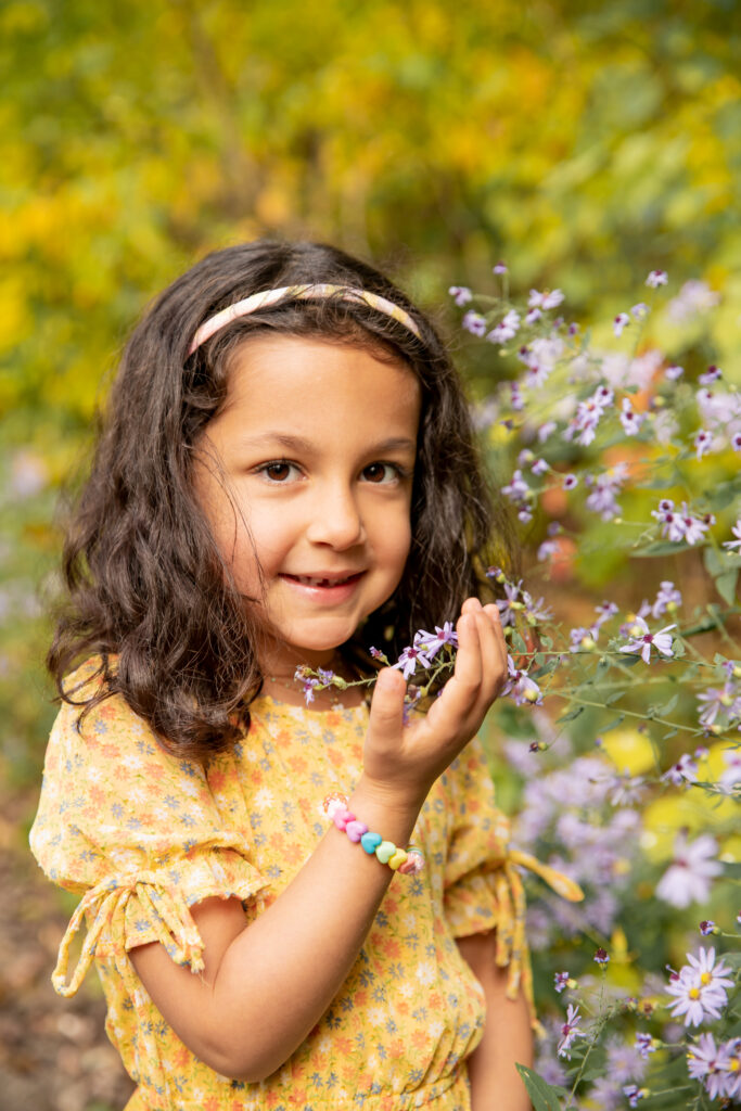 Girl stands with purple flowers looking at camera and smiles