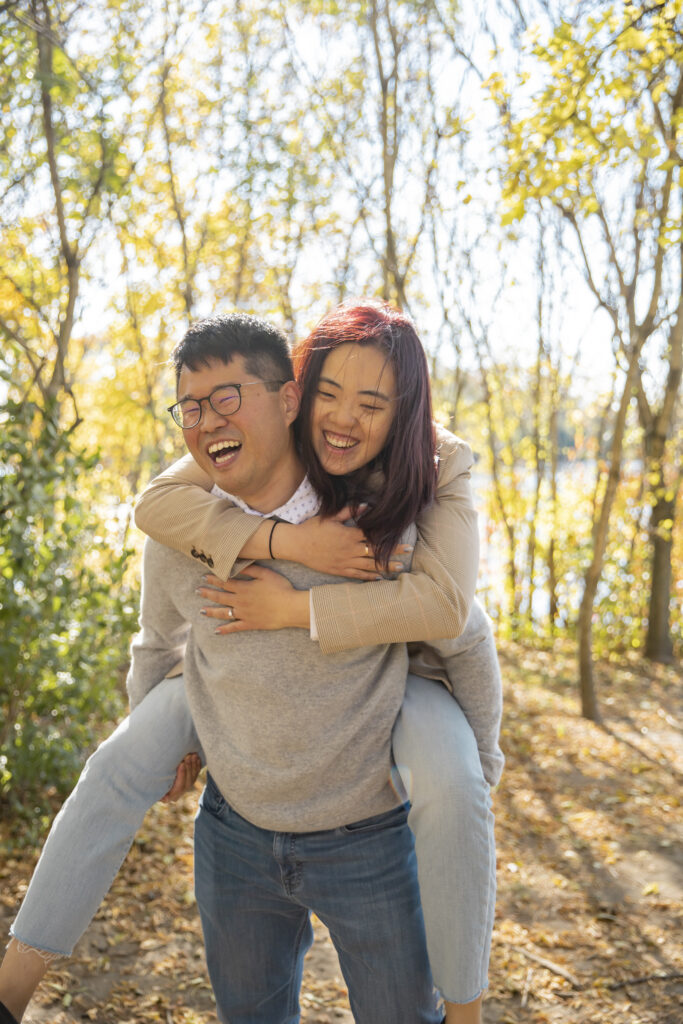 Couple laughs while woman does piggy back ride on fiance at Gallup Park in Ann Arbor Michigan