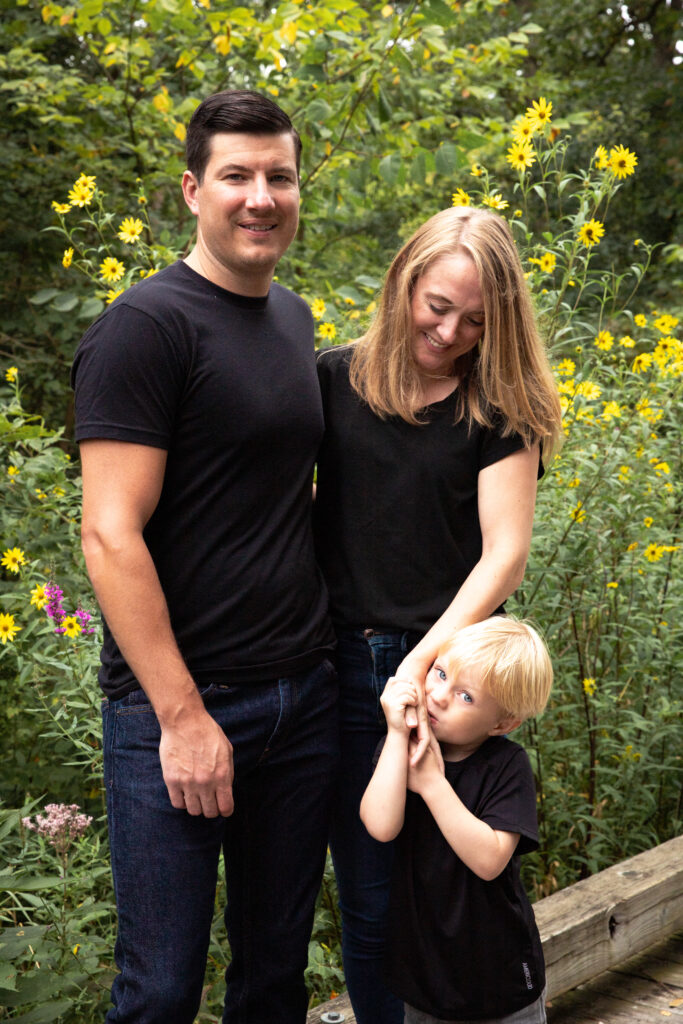 Family of three stands on boardwalk in front of wild flower patch at Mill Creek Park in Dexter Michigan