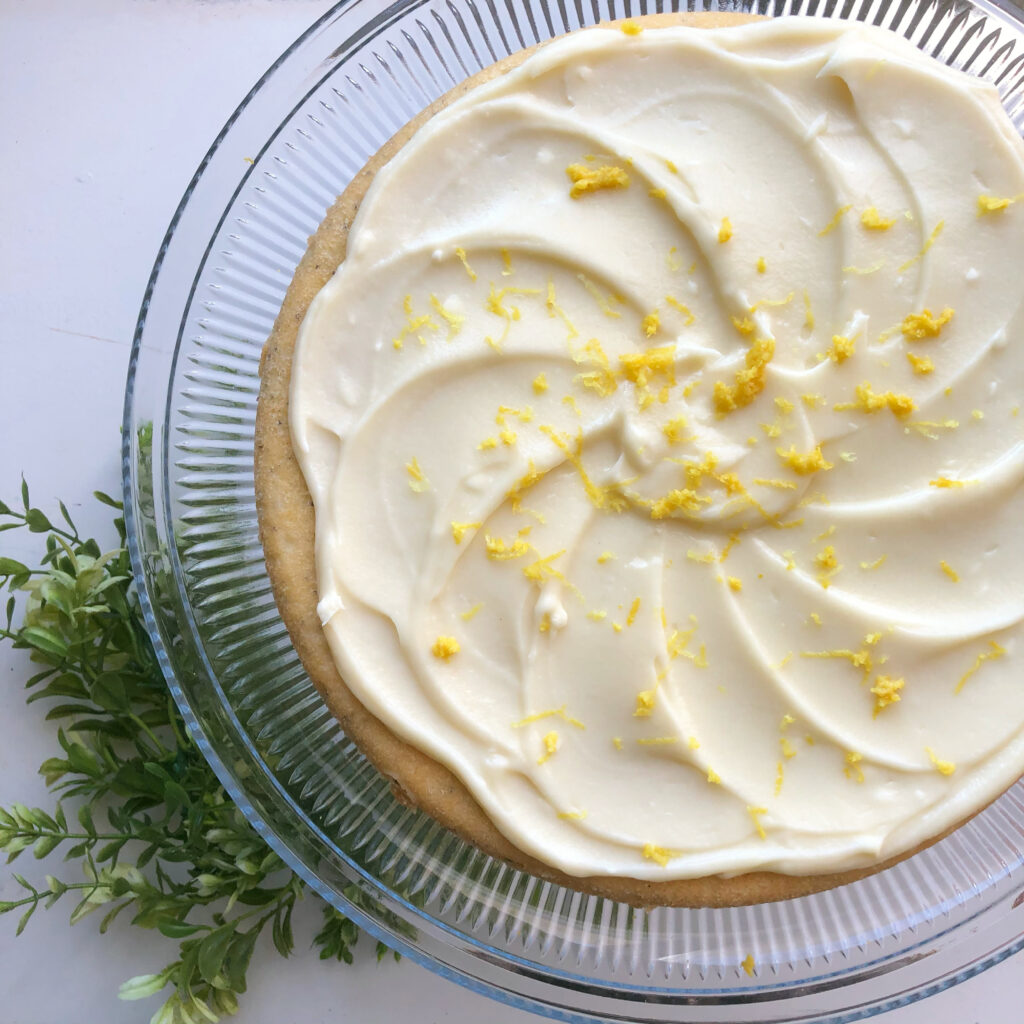 lemon poppyseed cake with cream cheese frosting and lemon zest on top on glass cake stand