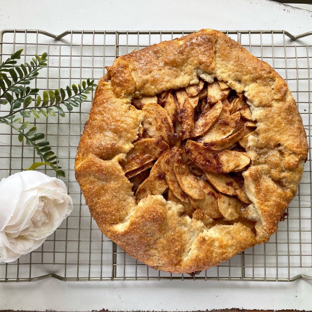 rustic apple tart on metal cooling rack with white rose and leaves