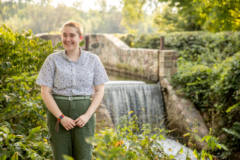 Senior stands in front of water fall and laughs off camera at sharon mills county park in manchester michigan