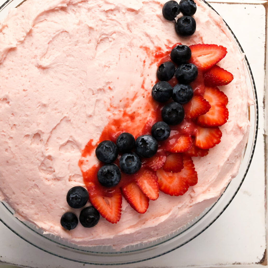 strawberry frosted cake with blueberries and sliced strawberries adorned on top