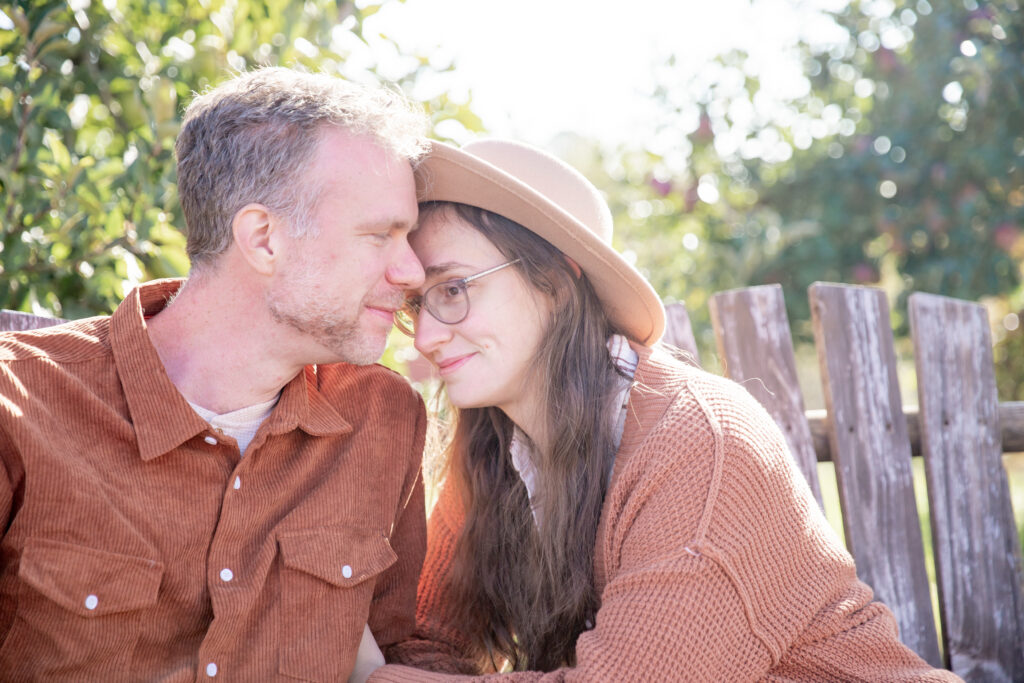 Husband and wife cuddle and smile on a swinging bench in the morning light at Alber Orchard and Cider Mill in Manchester Michigan