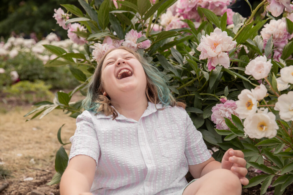 boy tosses his head back and laughs while sitting on the ground at the peony garden in the arb in ann arbor michigan