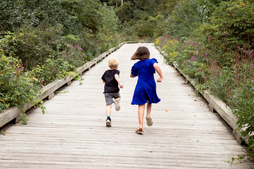 young girl and boy run away from camera on boardwalk