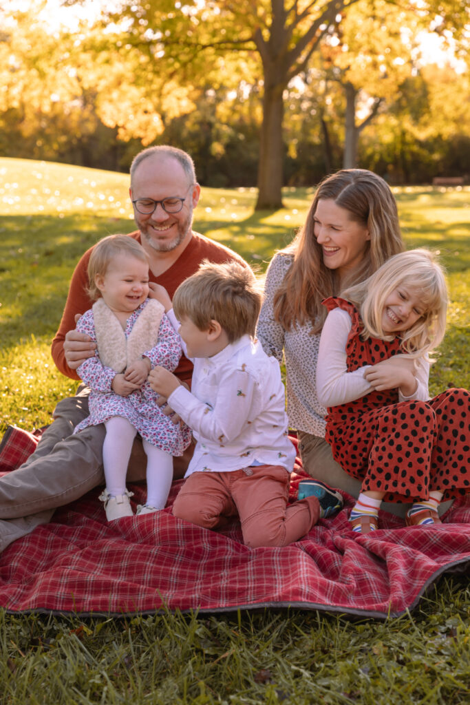 Family of 5 sits on blanket in fall and has a tickle fest while laughing together