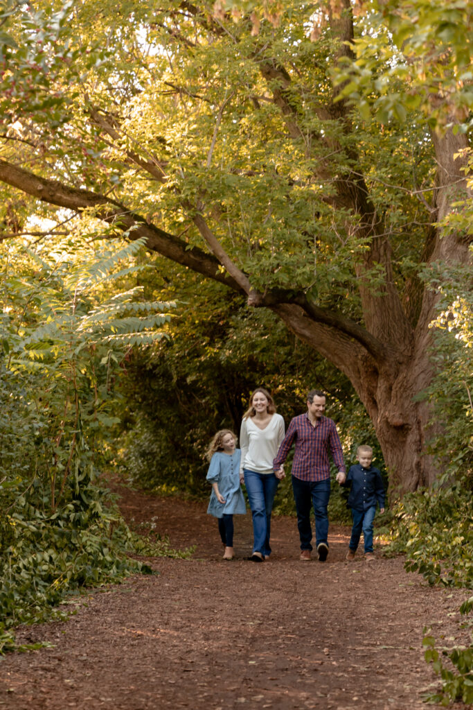 Family of four walks on path towards camera during golden hour at Gallup Park in Ann Arbor Michigan