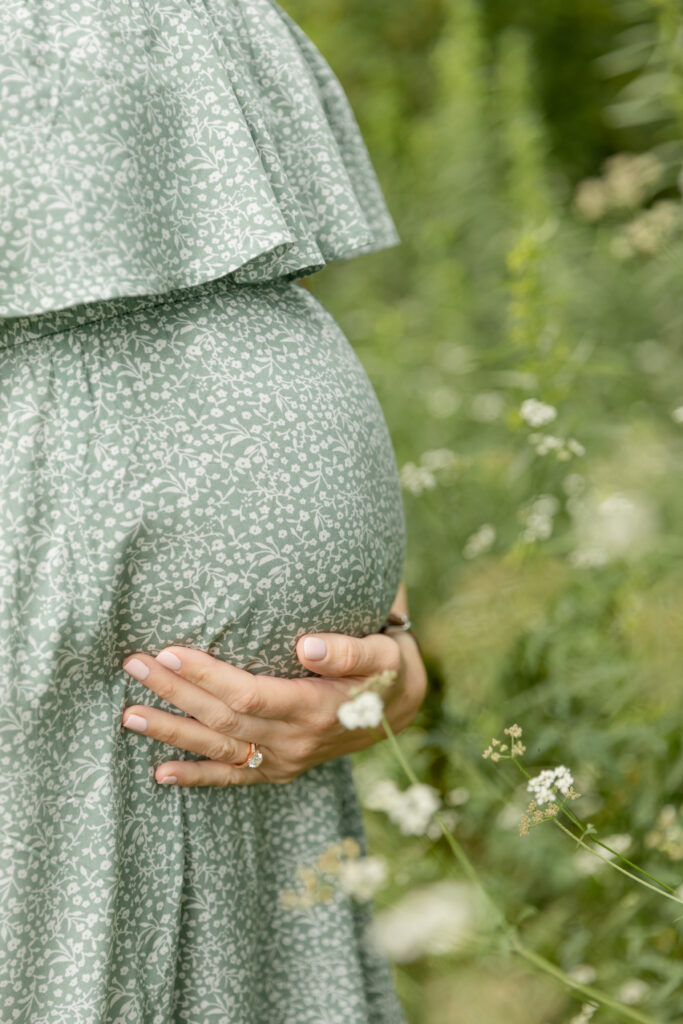 close up of pregnant woman holding her belly near white wild flowers at Saginaw Forest in Ann Arbor Michigan