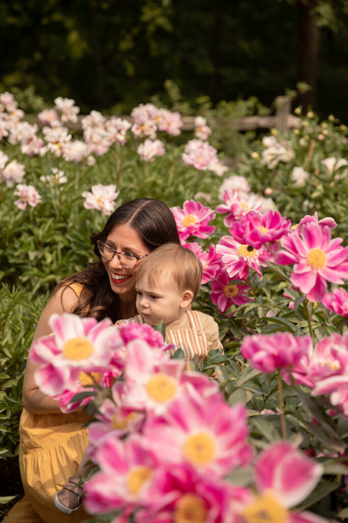 mother and toddler son smile and look off camera in peony garden at the arb in ann arbor michigan