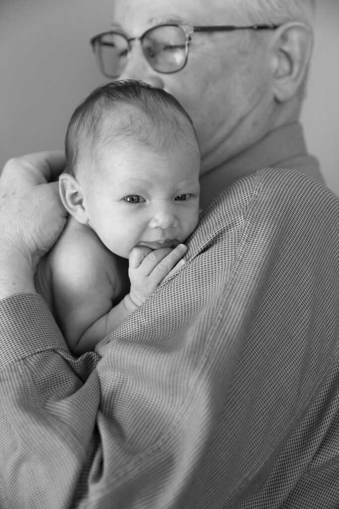 black and white photo of newborn looking over grandfather's shoulder