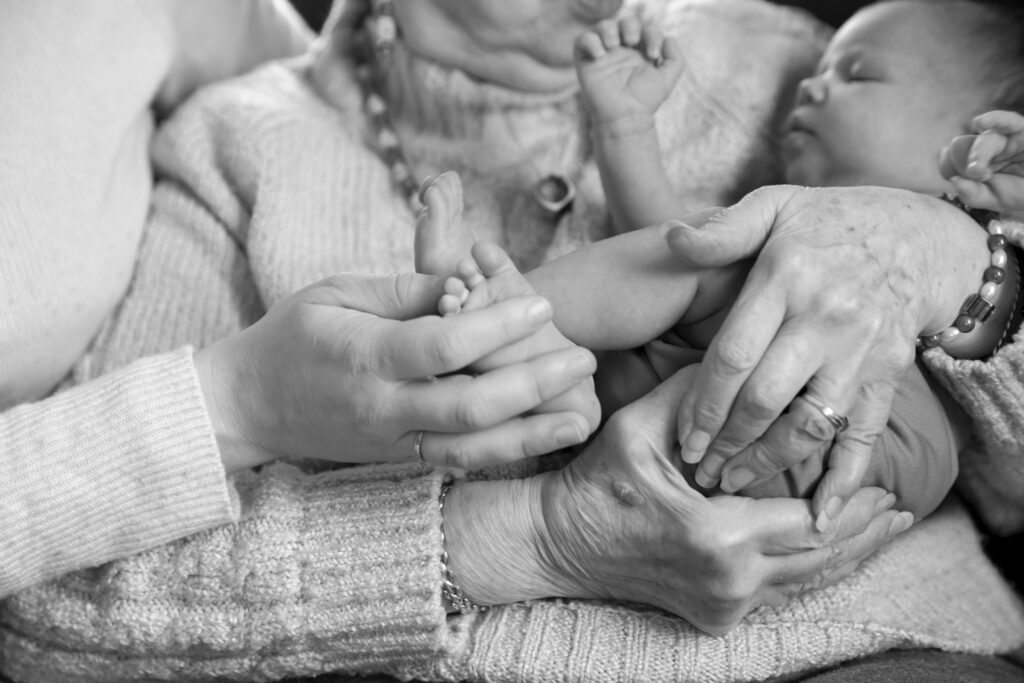 black and white photo close up of great grand grandmother holding newborn girl while mother holds baby's foot