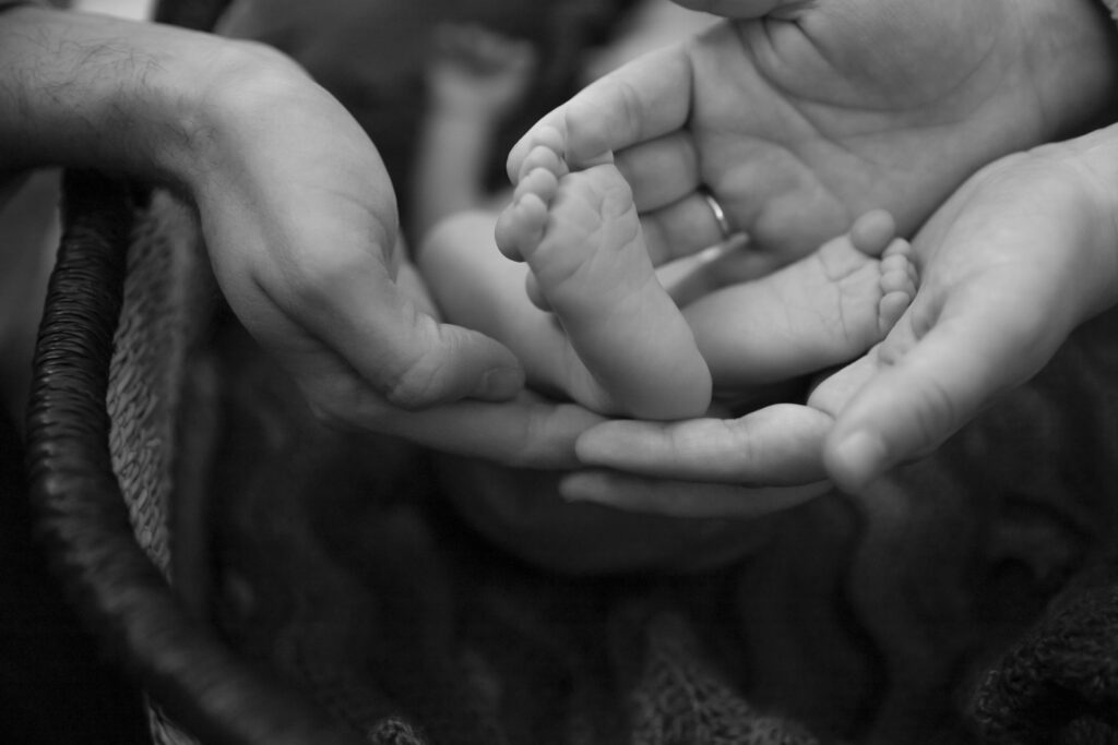 black and white photo close up of mother and father cupping newborn baby's feet