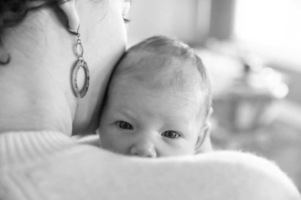 black and white photo of newborn looking over mother's shoulder