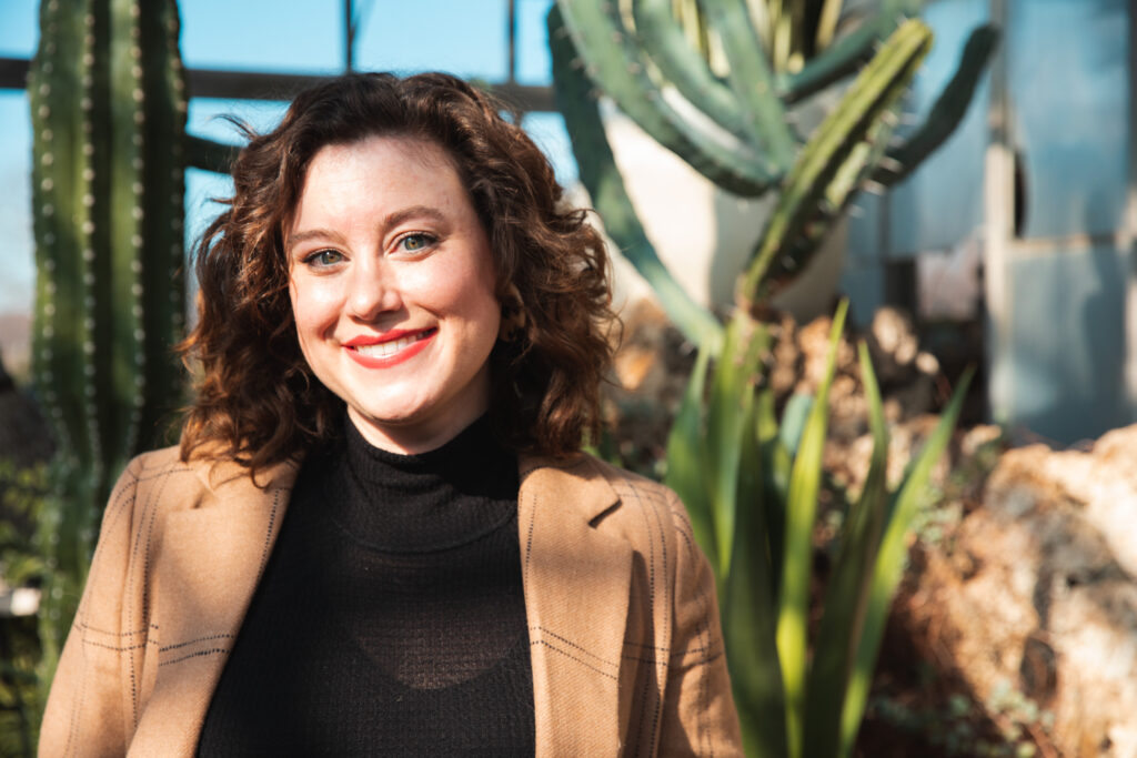 woman stands in arid cacti room and looks directly at camera during headshot session in belle isle conservatory in detroit michigan