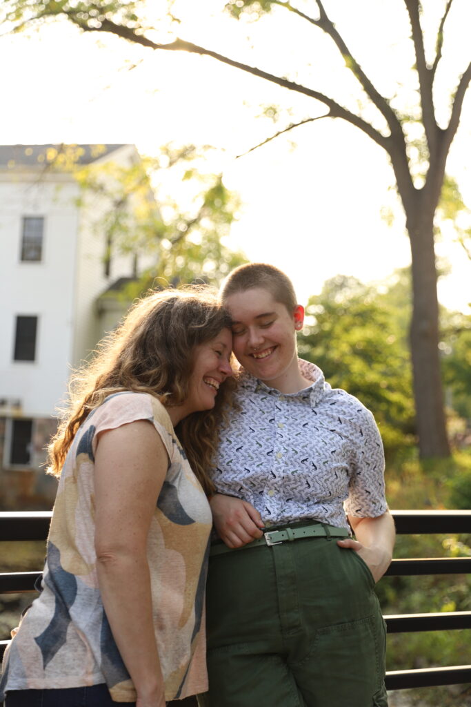 Raw photo of mother and adult child lean on railing, resting heads on each other and smile at Sharon Mills County Park in Manchester Michigan