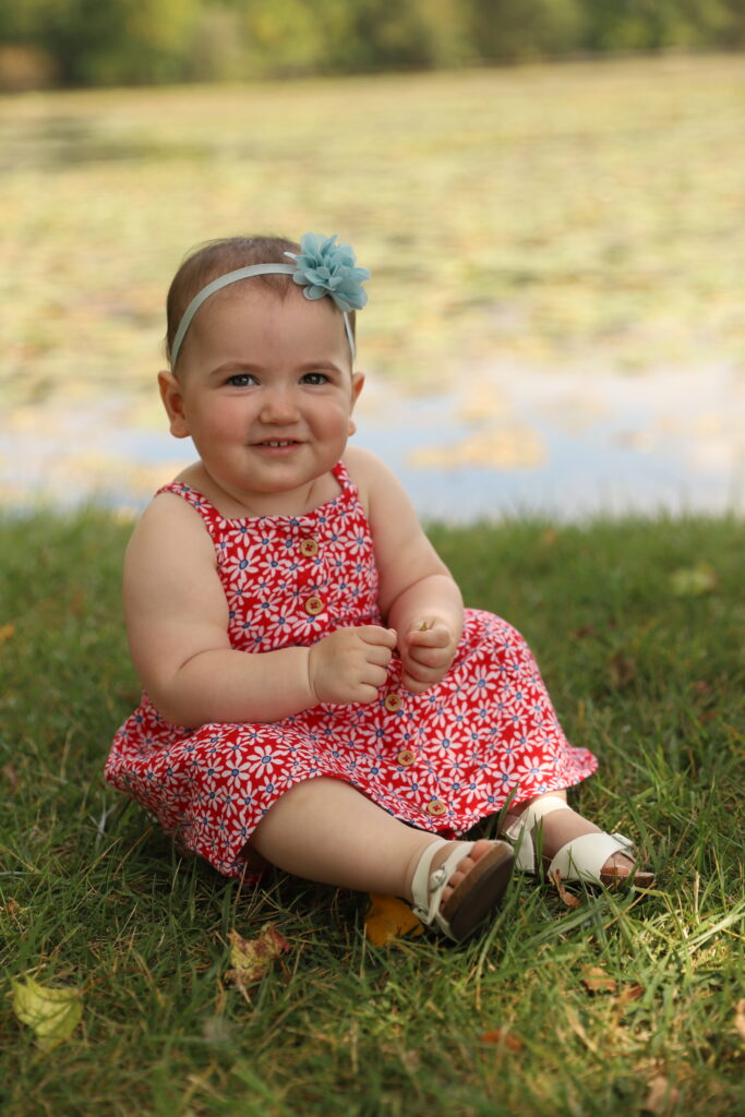 Raw photo of toddler girl sitting on grass in front of pond