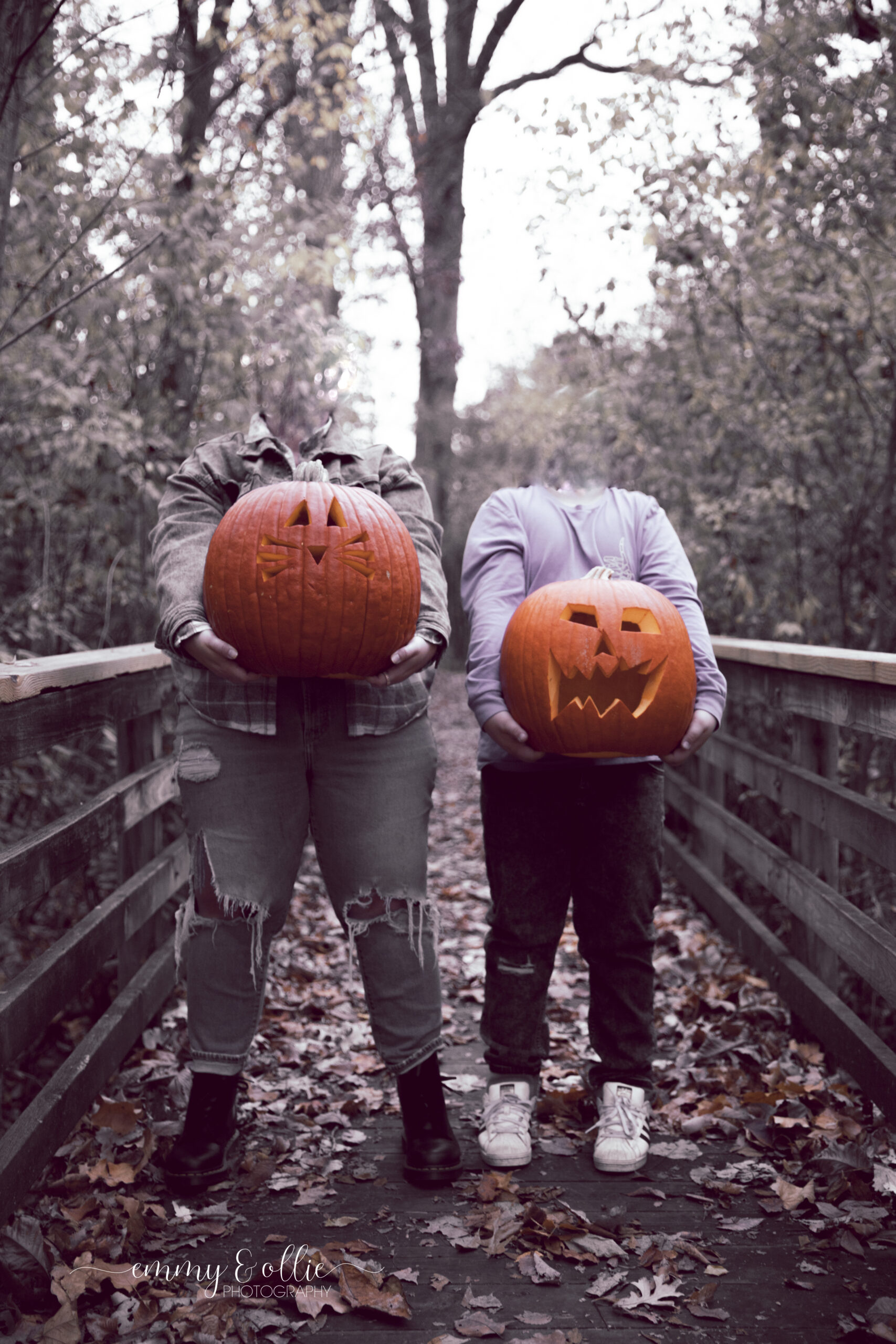 mother and son hold carved pumpkins in front of them on wooden bridge in the woods for halloween, heads digitally removed