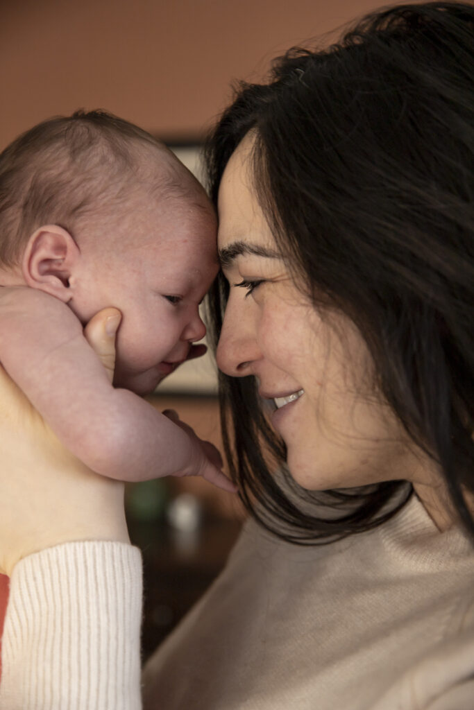 mother holds newborn baby up and touch foreheads