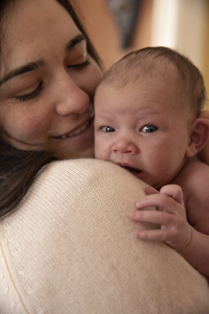 newborn baby looks over mother's shoulder towards camera