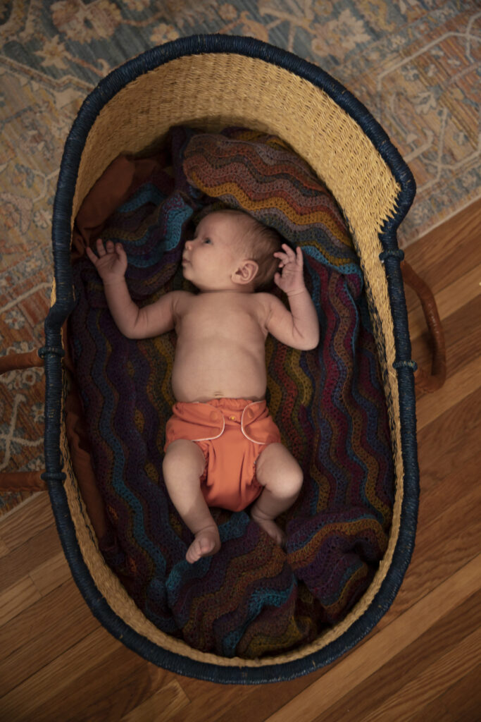 top down view of newborn baby laying in moses basket on beautiful crocheted blanket