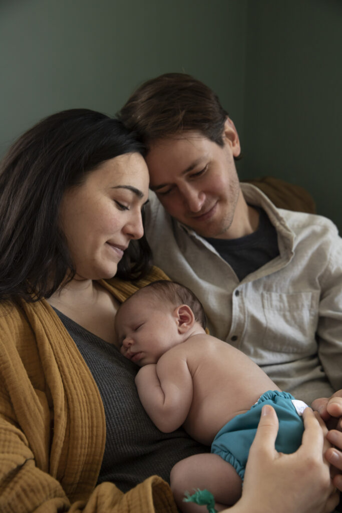 new mother and father cuddle and look down at newborn baby resting on mother's chest