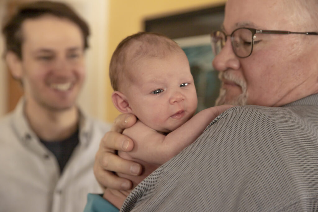 newborn baby looks over shoulder of grandfather