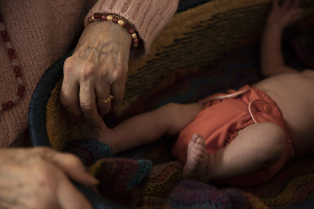 close up of great grandmother holding newborn baby's toes who is laying in Moses basket