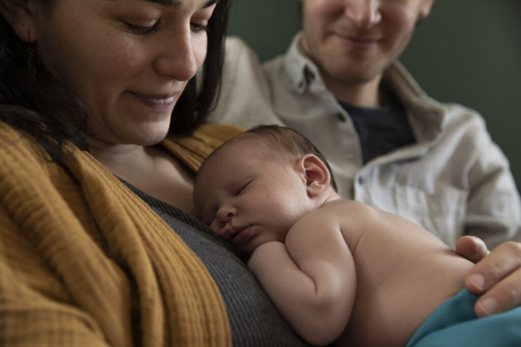 Mother smiles and looks down at sleeping newborn on chest