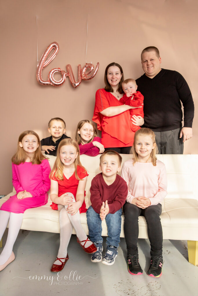 family poses and smiles in front of pink wall decorated with pink love balloon for valentine's day