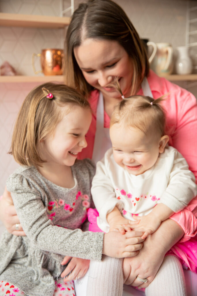 Mother sits with daughters in kitchen of studiostudio, all laughing