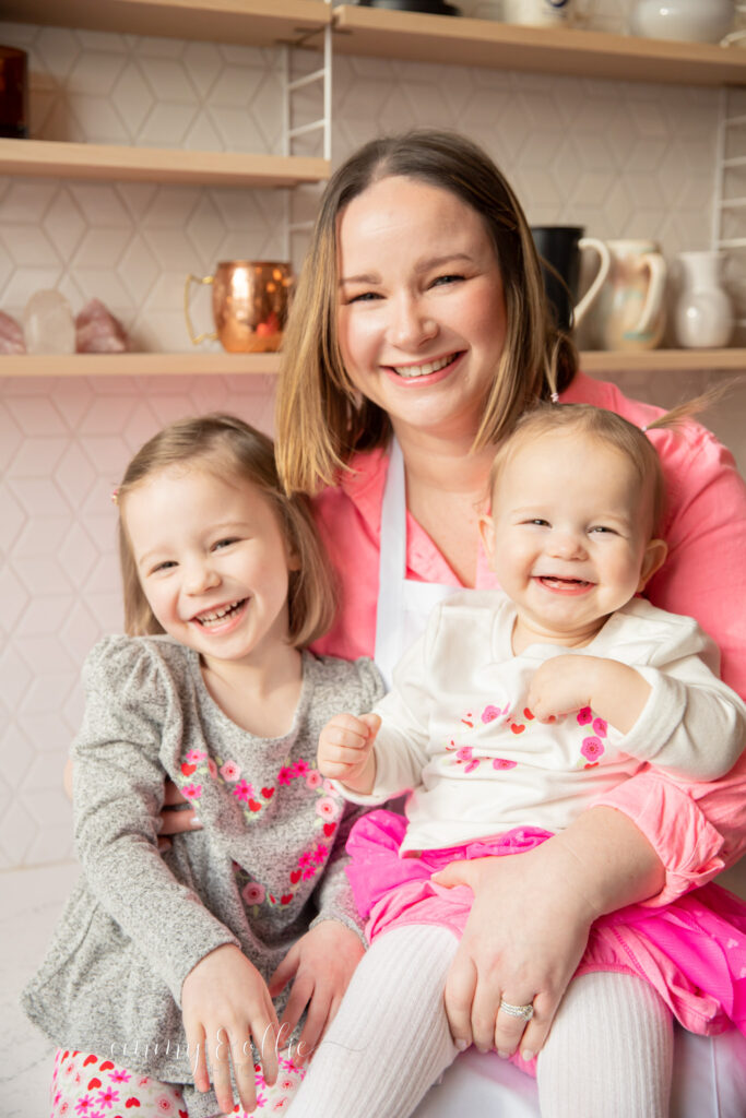 Mother sits with daughters in kitchen of studiostudio, all laughing and smiling at camera