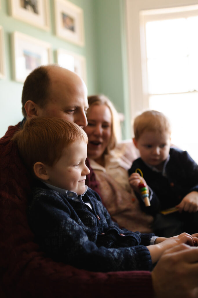 family of four reads book together on chair in reading nook