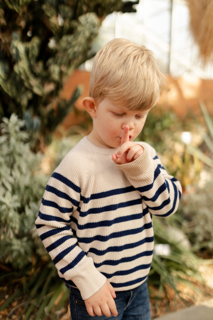 toddler boy signs shh with finger in front of cacti at the matthaei botanical gardens in ann arbor michigan