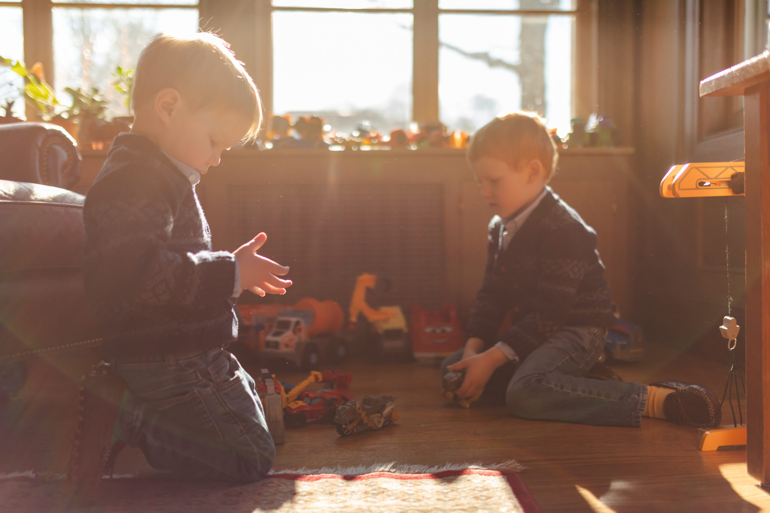 young brothers play with trucks on the ground in sun filled sunroom