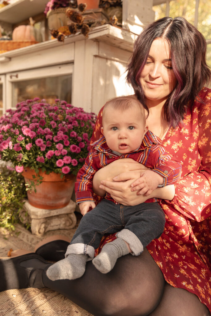 mother sits with baby in greenhouse decorated for fall at rustic wild arrow in brooklyn michigan