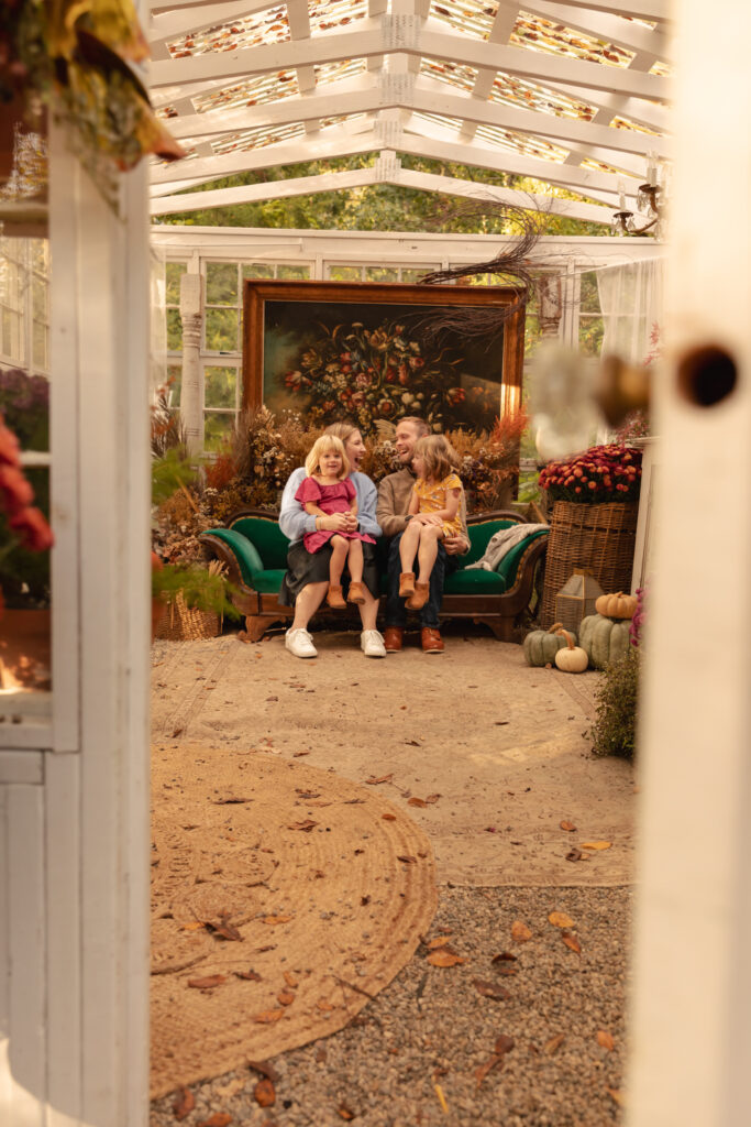 family of four sits on beautiful antique green couch in greenhouse decorated for fall at rustic wild arrow in brooklyn michigan