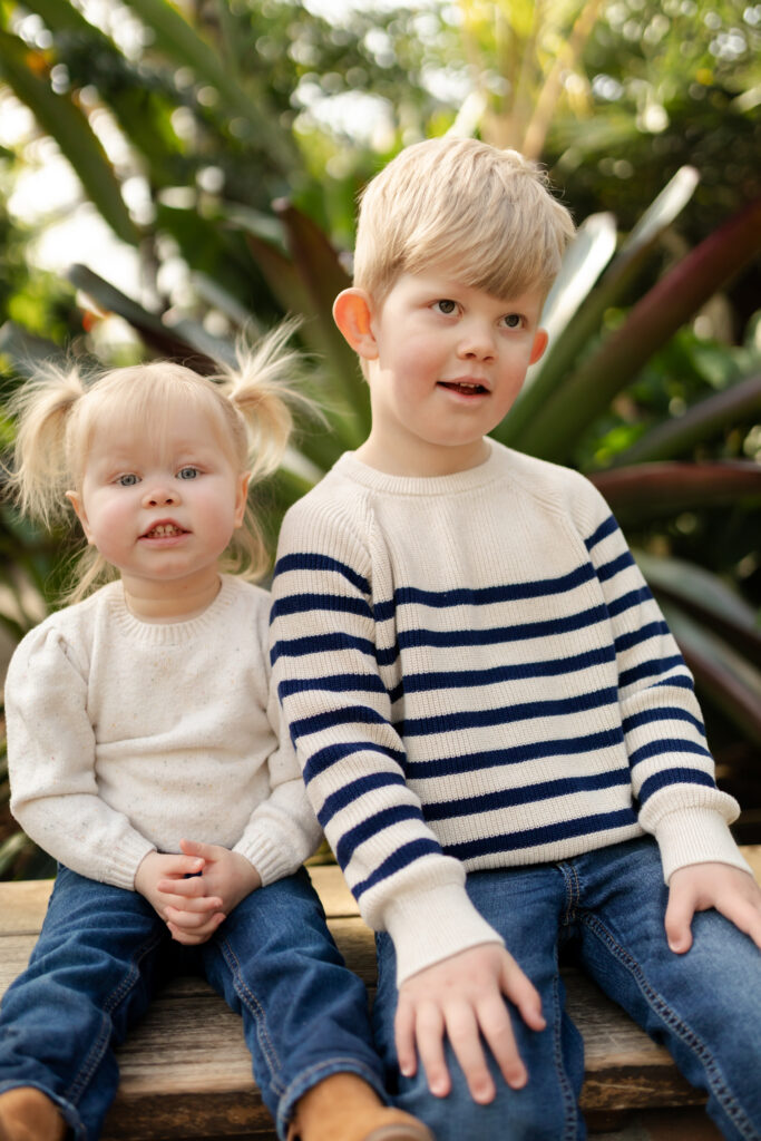 young sister and brother sit on bench together in conservatory at matthaei botanical gardens in ann arbor michigan