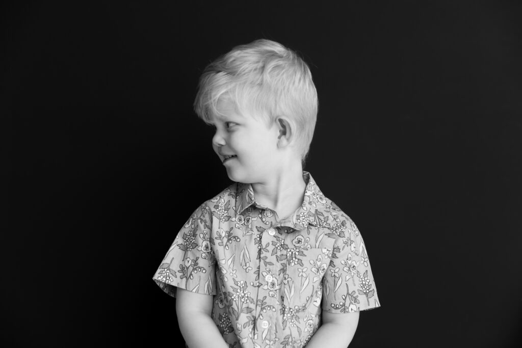 Portrait of a toddler boy in black and white against a black background as he looks off camera to the left of frame