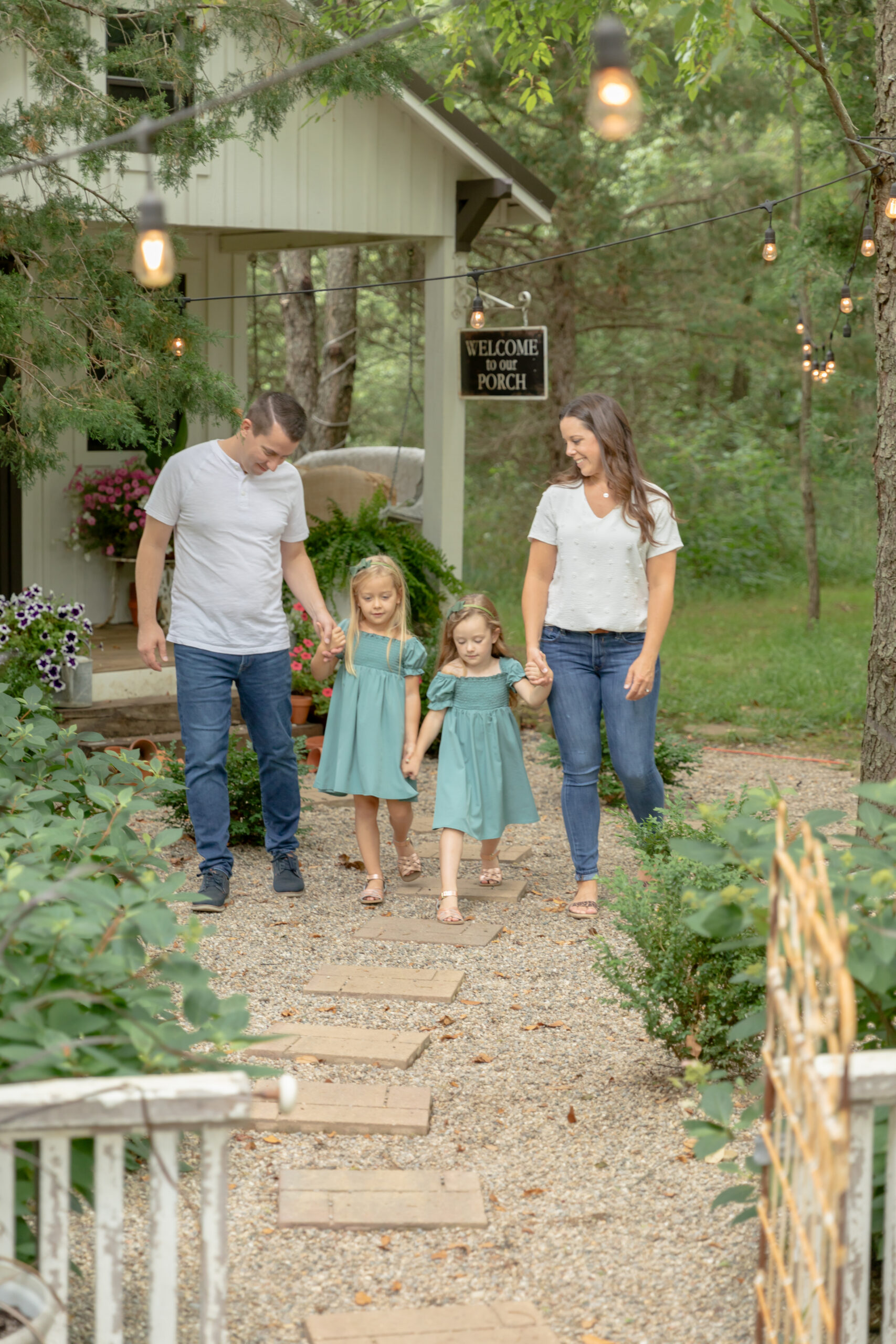 Family of four walks towards the camera while smiling along paving stones in a garden at Rustic Wild Arrow in Brooklyn, Michigan