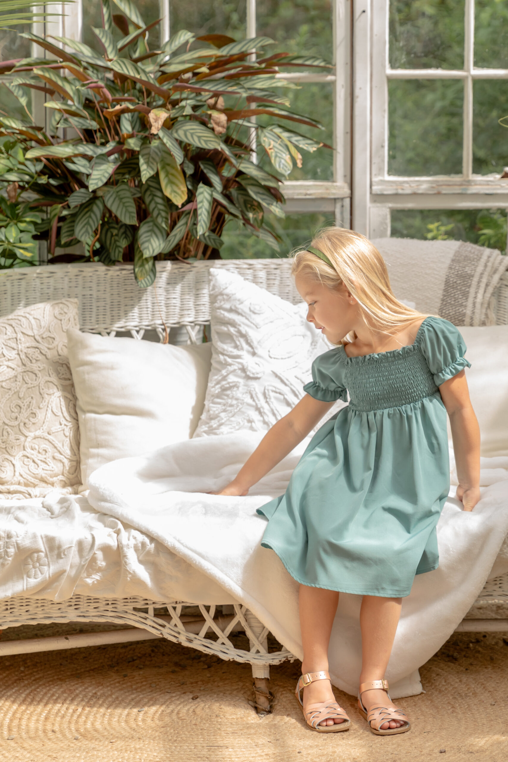 Young girl sits on a white wicker couch in a beautiful greenhouse at Rustic Wild Arrow in Brooklyn, Michigan