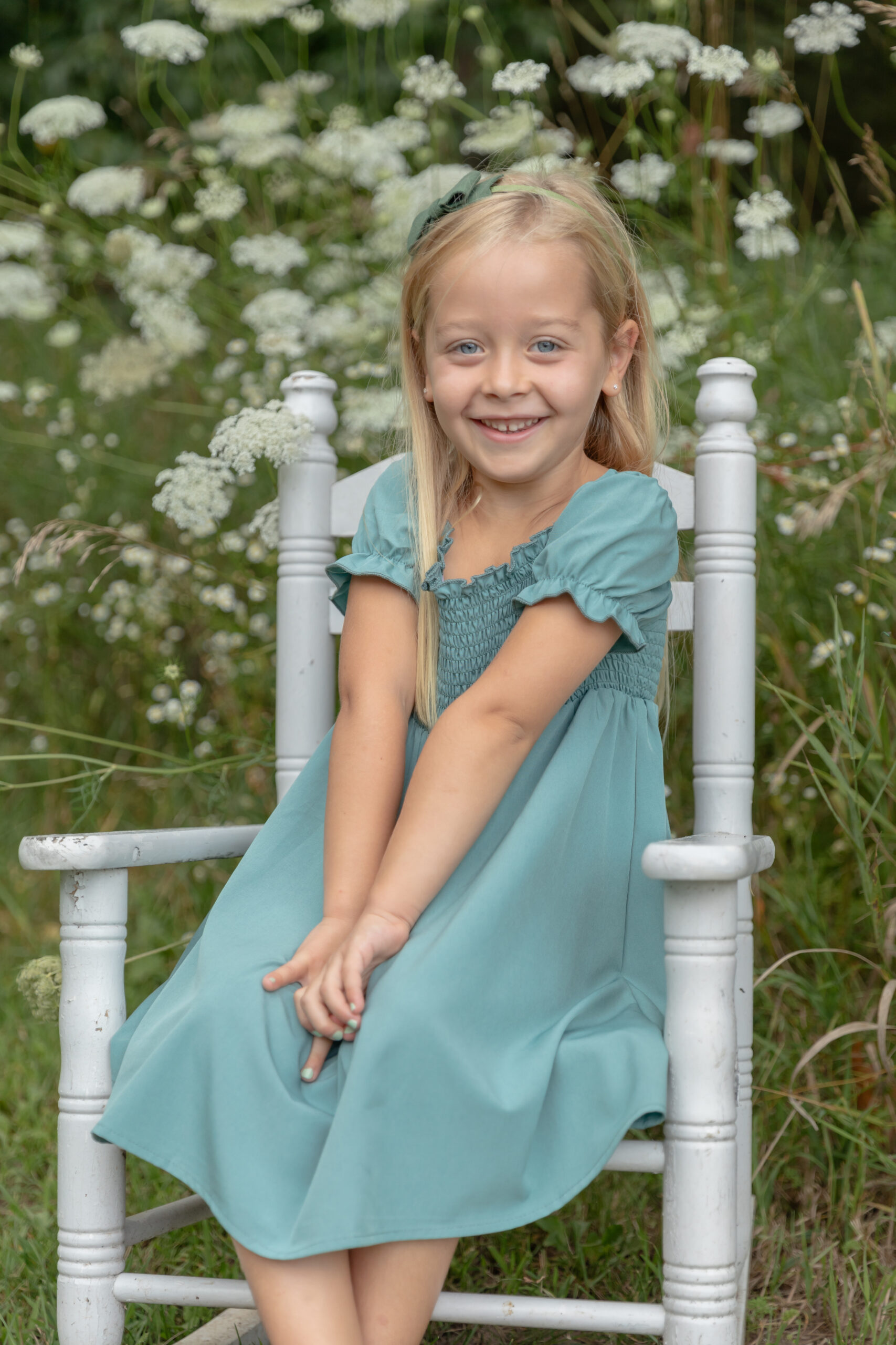 Young girl poses in a small white rocking chair in a field of Queen Anne's Lace at Rustic Wild Arrow in Brooklyn, Michigan