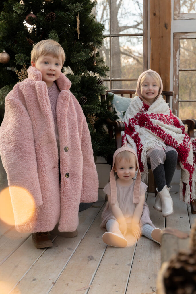 Three children sit together smiling at the camera in a greenhouse decorated for Christmas