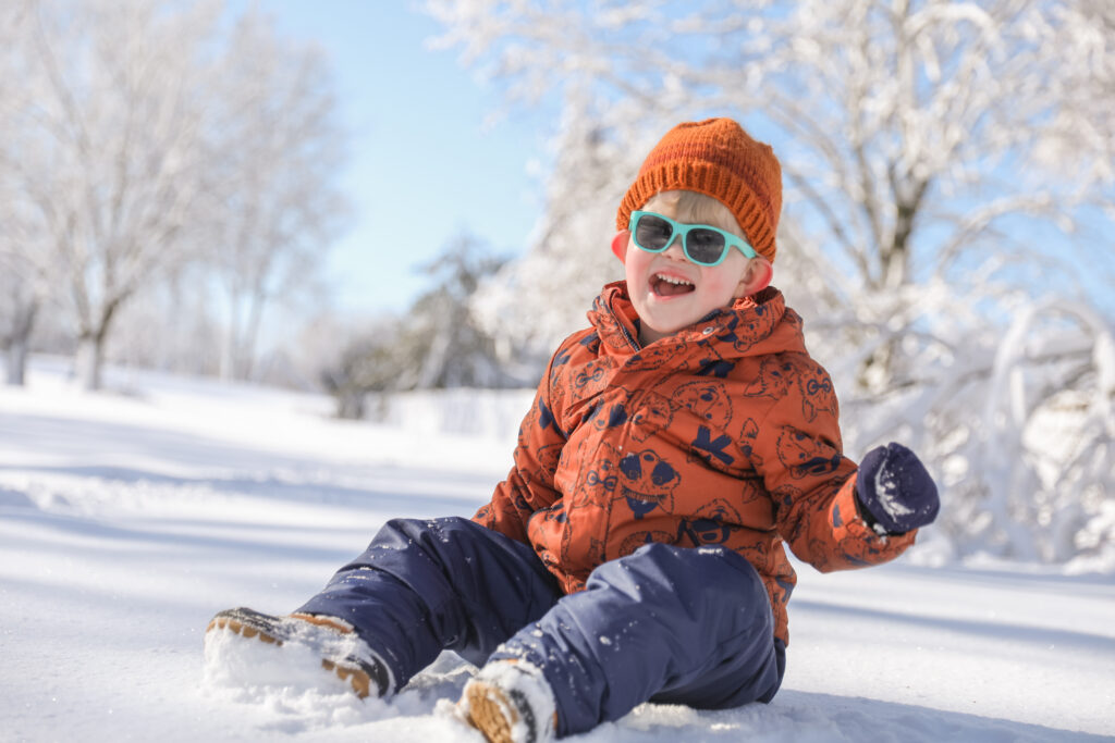 Toddler boy laughs while playing in the snow on a bright day