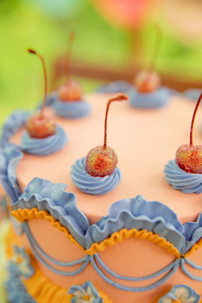 A beautiful cake by Sweet Heather Anne with peach, orange, and lavender colored frosting and red glittery cherries on top