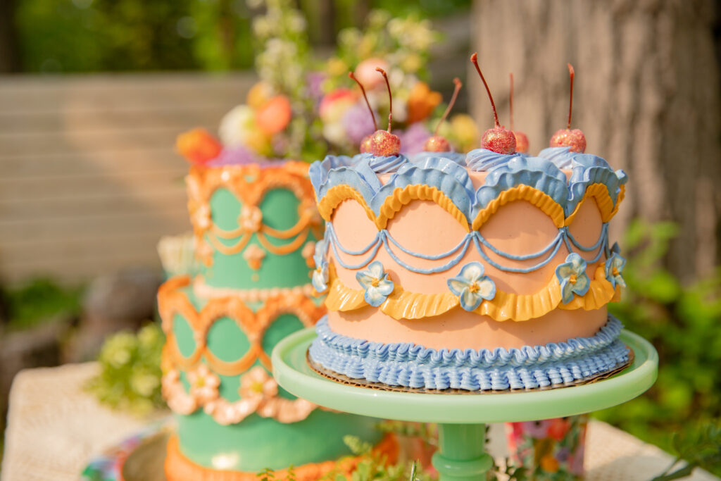 Two beautifully decorated cakes sit on a table outside with beautiful flowers in the background