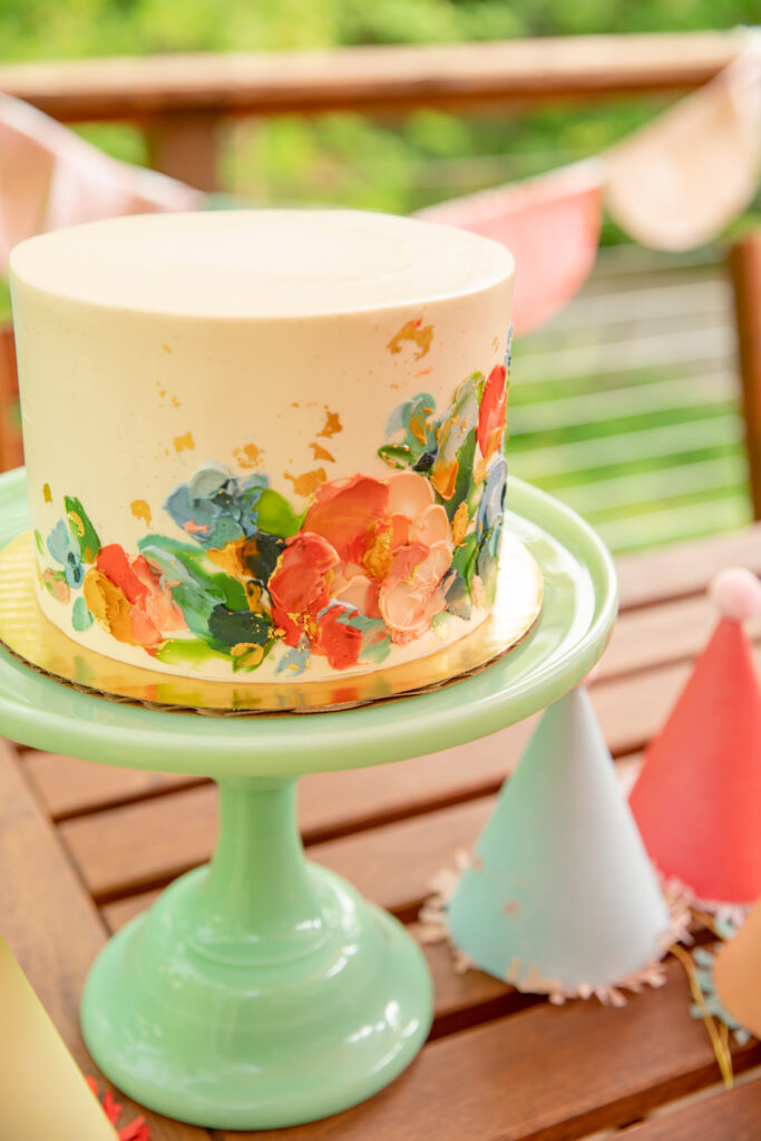 A beautiful cake by Sweet Heather Anne sits on a green milk glass stand with party hats sitting around